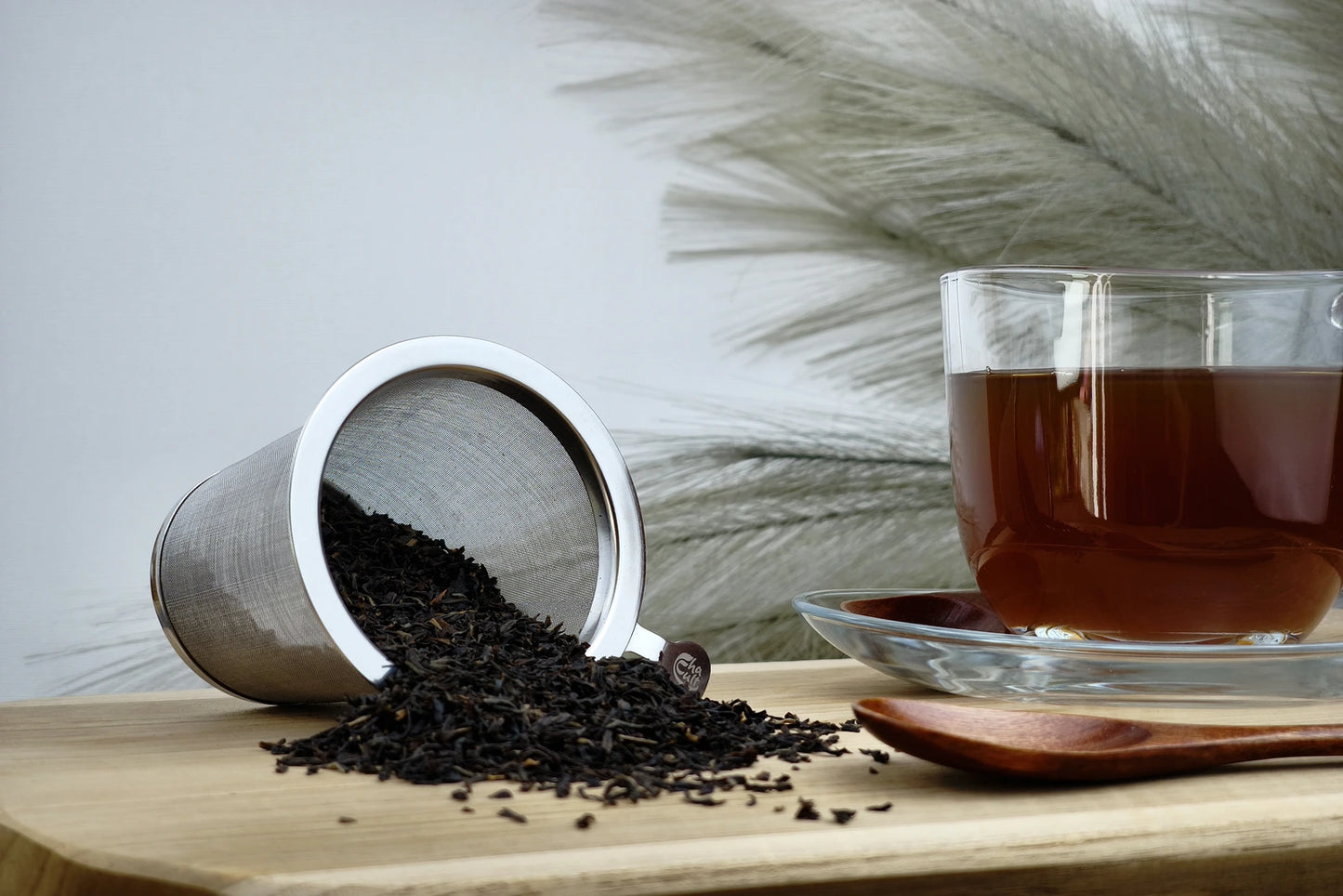 Schwarzer Tee Assam FTGFOP1 Bio in Teetasse mit Löffel, dunkelbrauner Aufguss, loser Tee im Sieb