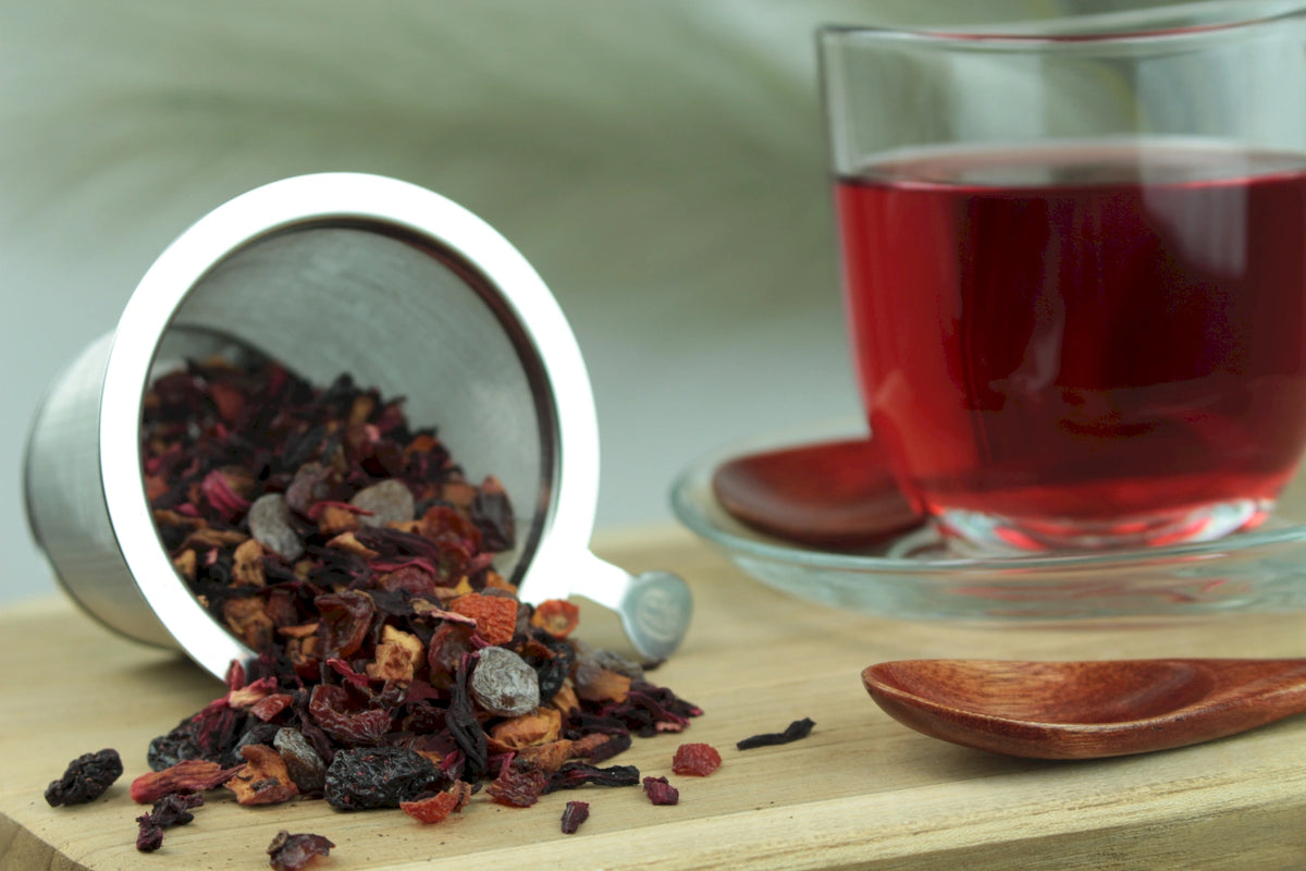 Produktfoto einer Tasse Tee und losen Teeblättern von Wildkirsche, aromatisierte Früchteteemischung mit intensivem Kirschgeschmack.