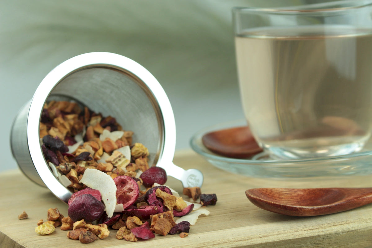 Produktfoto einer Tasse Tee und losen Teeblättern von Wolkenschieber, Früchteteemischung mit Kirsche, Kiwi und Kokos.