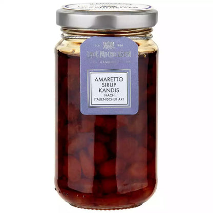 Ein Glas mit Amaretto Kandis in dunklem Sirup steht frontal fotografiert, der Deckel ist silberfarben und das Etikett zeigt die Geschmacksrichtung.