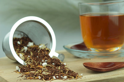 Früchtetee Ananas Zitronen Sorbet, loser Früchtetee im Teesieb, Teetasse mit goldgelbem Aufguss und Holzlöffel auf Holzuntergrund