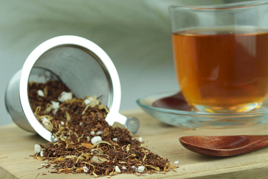 Früchtetee Ananas Zitronen Sorbet, loser Früchtetee im Teesieb, Teetasse mit goldgelbem Aufguss und Holzlöffel auf Holzuntergrund