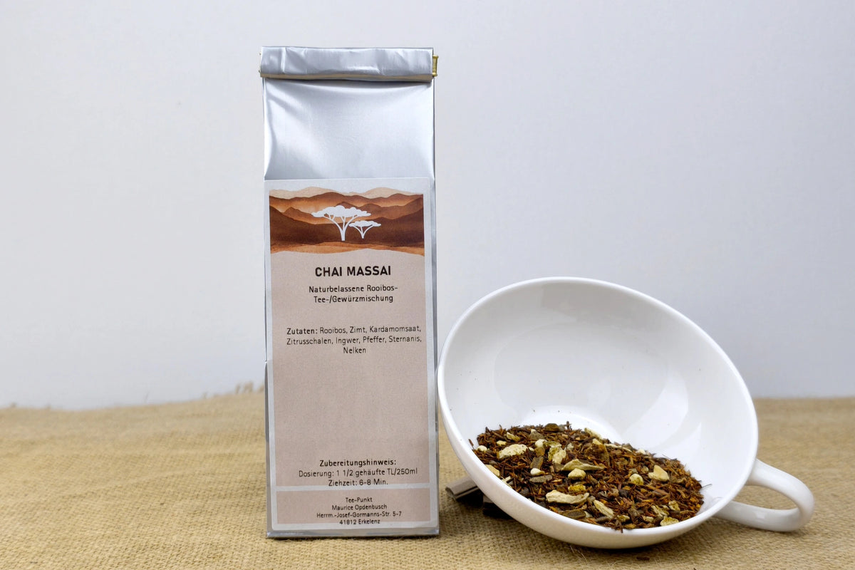 Silberne Packung Chai Massai Rooibos-Gewürztee neben einer weißen Tasse mit losem Rooibostee und Gewürzen.