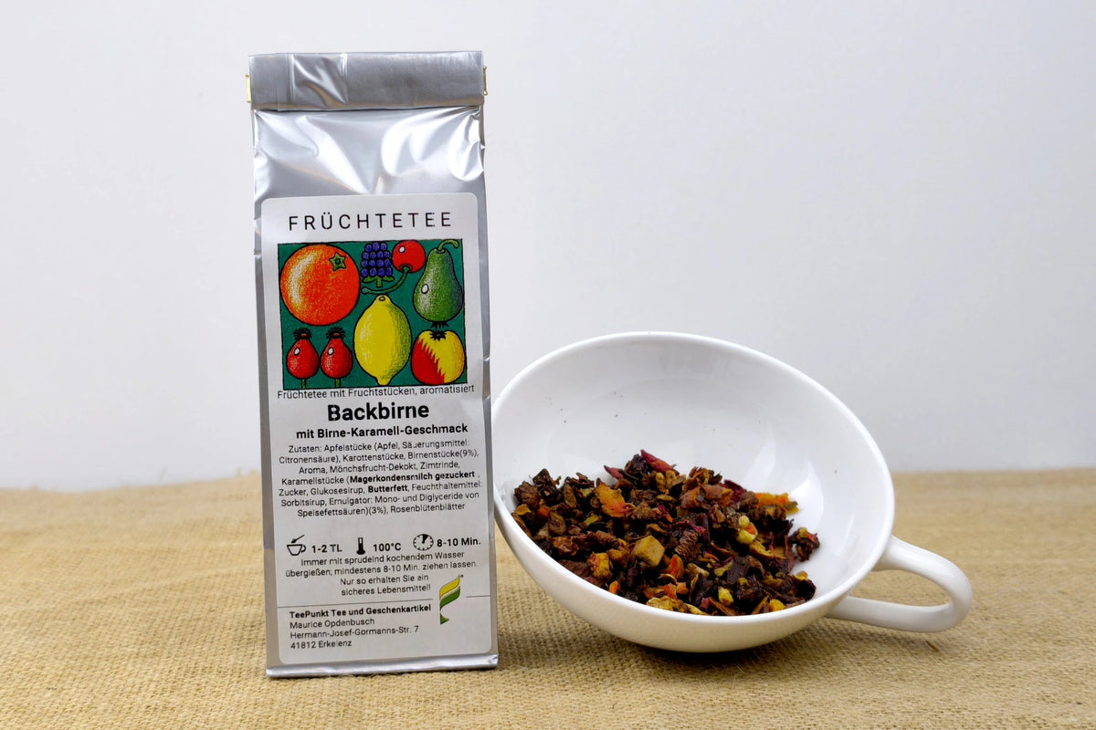 Silberne Packung Backbirne Früchtetee mit Birne-Karamell-Geschmack neben einer weißen Tasse mit losem Früchtetee.
