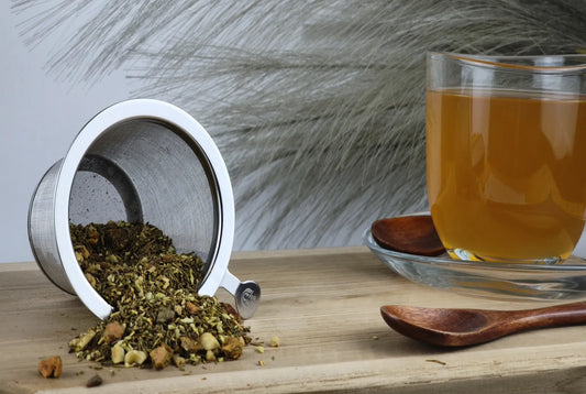 Matcha Haselnuss Tee in Teetasse, goldgelber Aufguss, loser Tee mit Haselnussstücken im Sieb