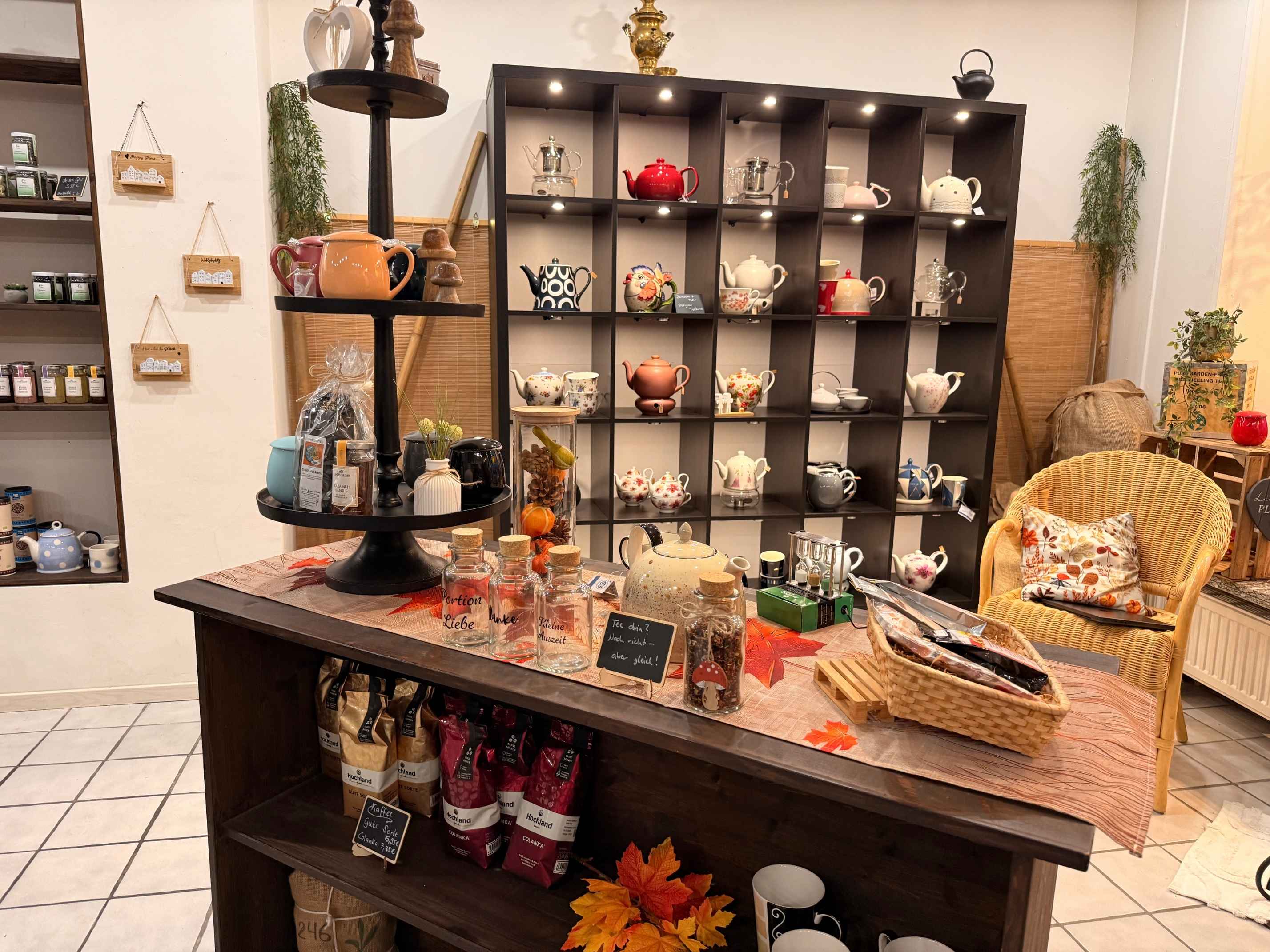 Regal mit verschiedenen Teekannen und Teezubehör im Fachgeschäft TeePunkt Erkelenz, herbstlich dekorierter Verkaufstisch mit Tee und Geschenkideen.
