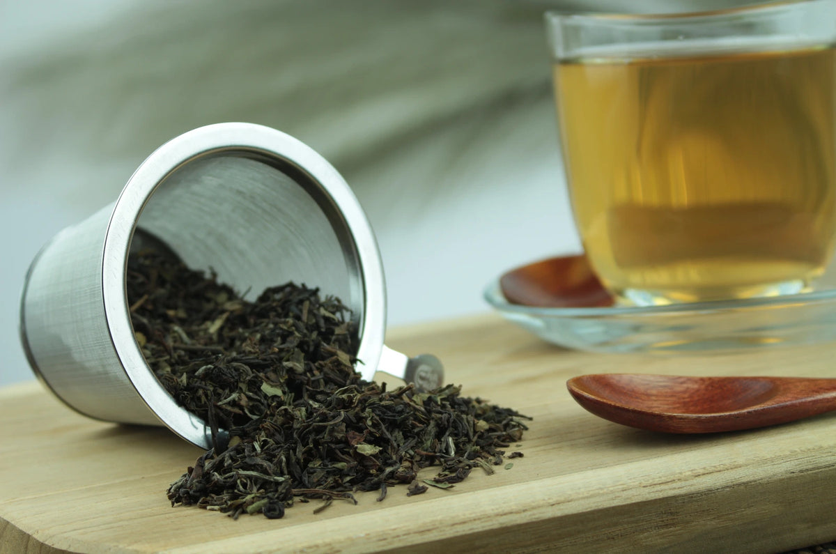 Produktfoto einer Tasse Tee und der Verpackung von Darjeeling FTGFOP1 Inbetween Tea of the Year, blumig und fein.