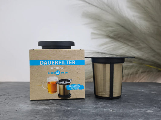 Produktfoto der Verpackung und des Dauerfilters mit Deckel in Schwarz, Größe M (Ø 6 cm), aus Kunststoff und Edelstahlgewebe.