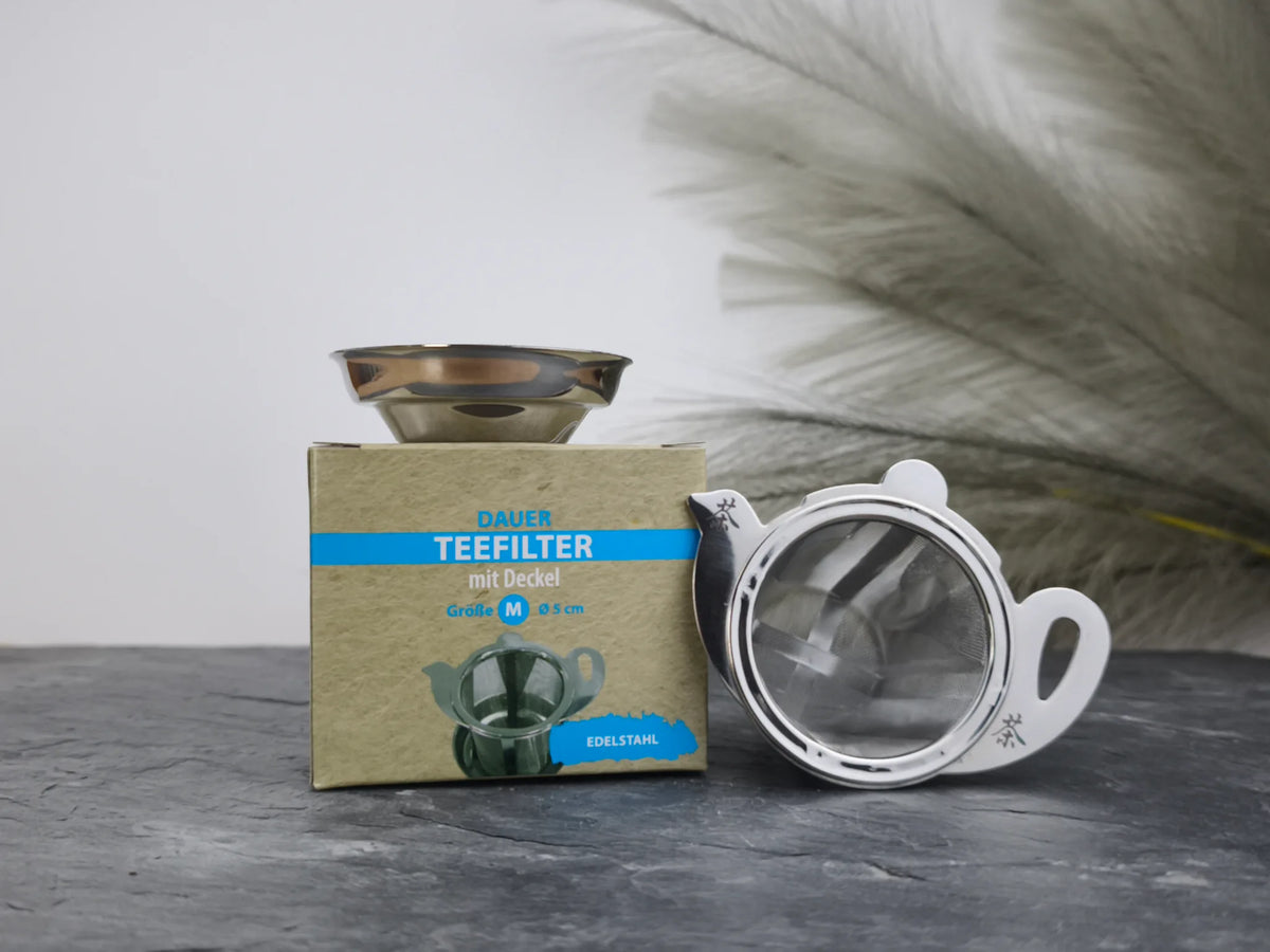 Produktfoto der Verpackung und des Dauerfilters „Teekanne“ mit Deckel, Größe M (Ø 6 cm), ein hochwertiger Edelstahl-Teefilter mit Abtropfschale.