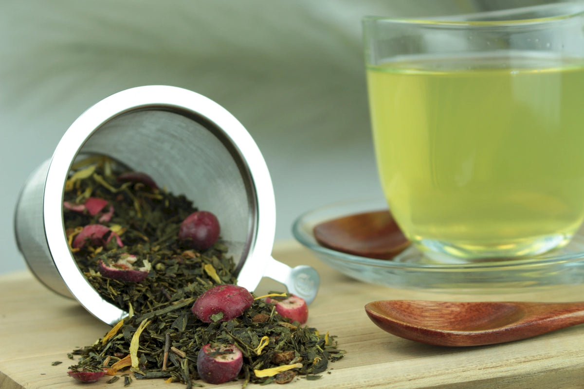 Produktfoto einer Tasse Tee und losen Teeblättern von Grüner Tee Sanddorn Cranberry, fruchtig und erfrischend.