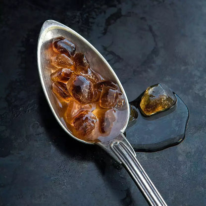 Braune Kandisstücke in Sirup auf einem silbernen Löffel mit Kandis-Sirup auf dunklem Hintergrund, Nahaufnahme
