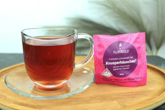 Produktfoto einer Tasse Tee und der Verpackung von Knusperhäuschen, festlicher Genuss mit gebrannter Mandel, milder Früchtetee.