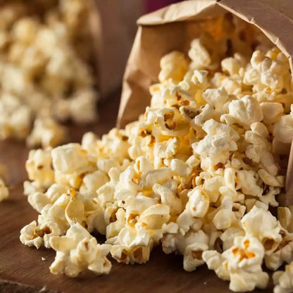 Geröstetes Popcorn fällt aus einer Papiertüte auf einen Holztisch