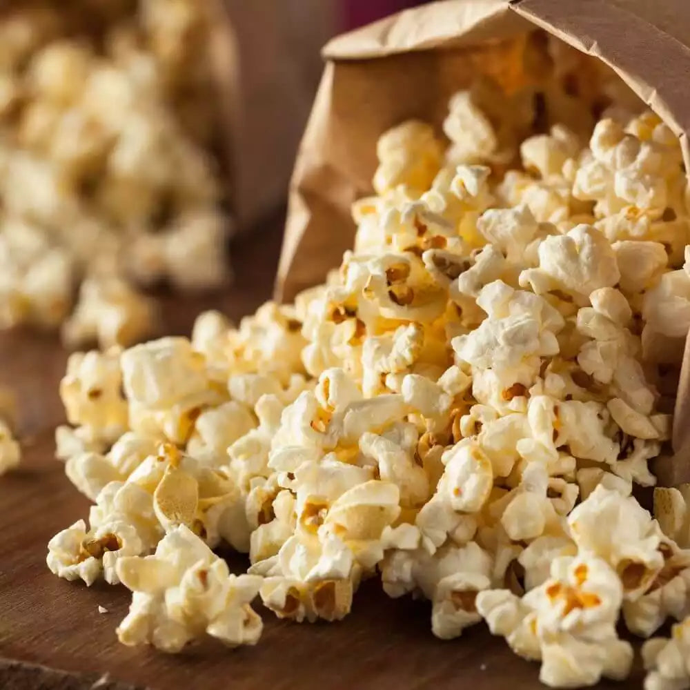 Geröstetes Popcorn fällt aus einer Papiertüte auf einen Holztisch