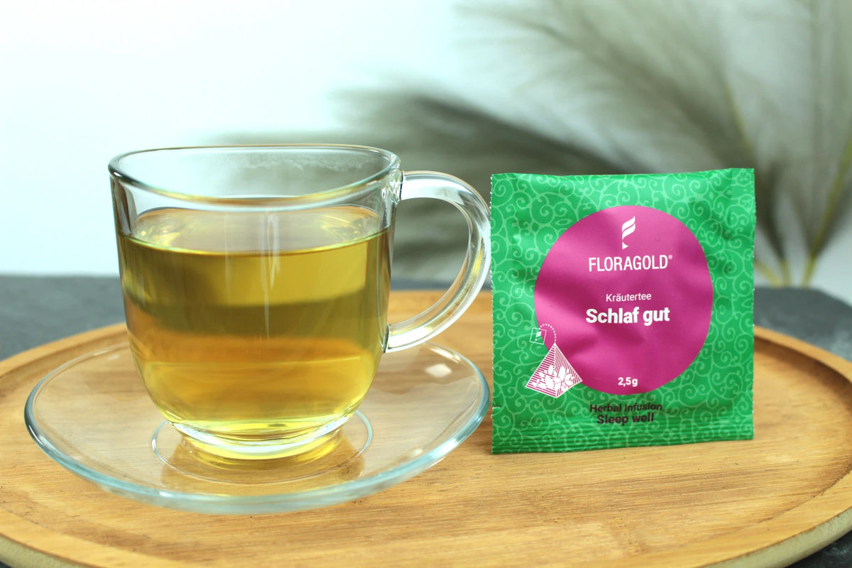 Produktfoto einer Tasse Tee und der Verpackung von Schlaf Gut, entspannender Kräutertee für die Nacht.