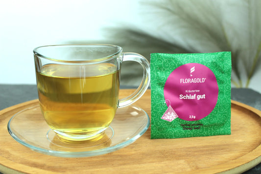 Produktfoto einer Tasse Tee und der Verpackung von Schlaf Gut, entspannender Kräutertee für die Nacht.