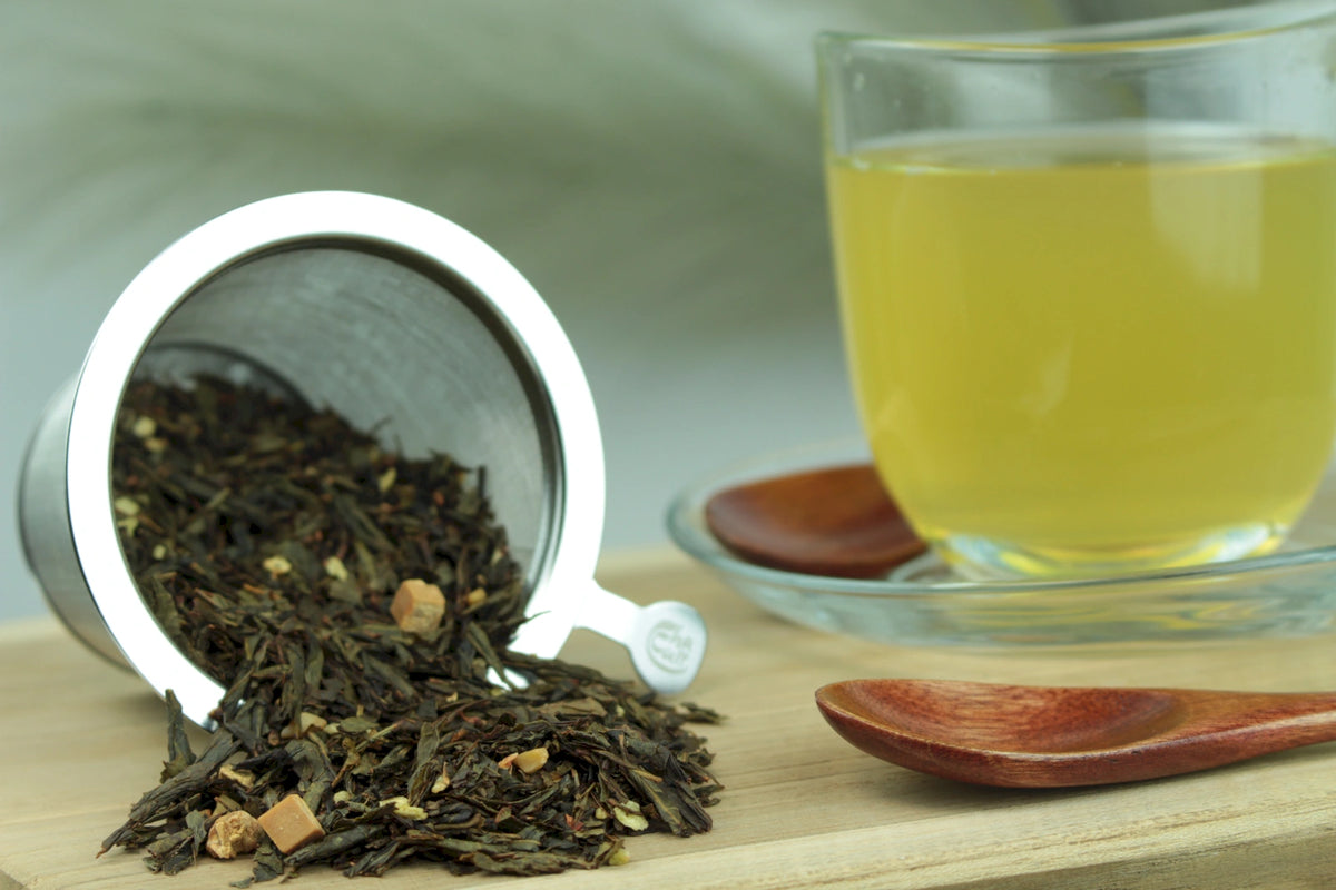 Produktfoto einer Tasse Tee und losen Teeblättern von Sencha Mandelmilch, aromatisierte Grünteemischung.