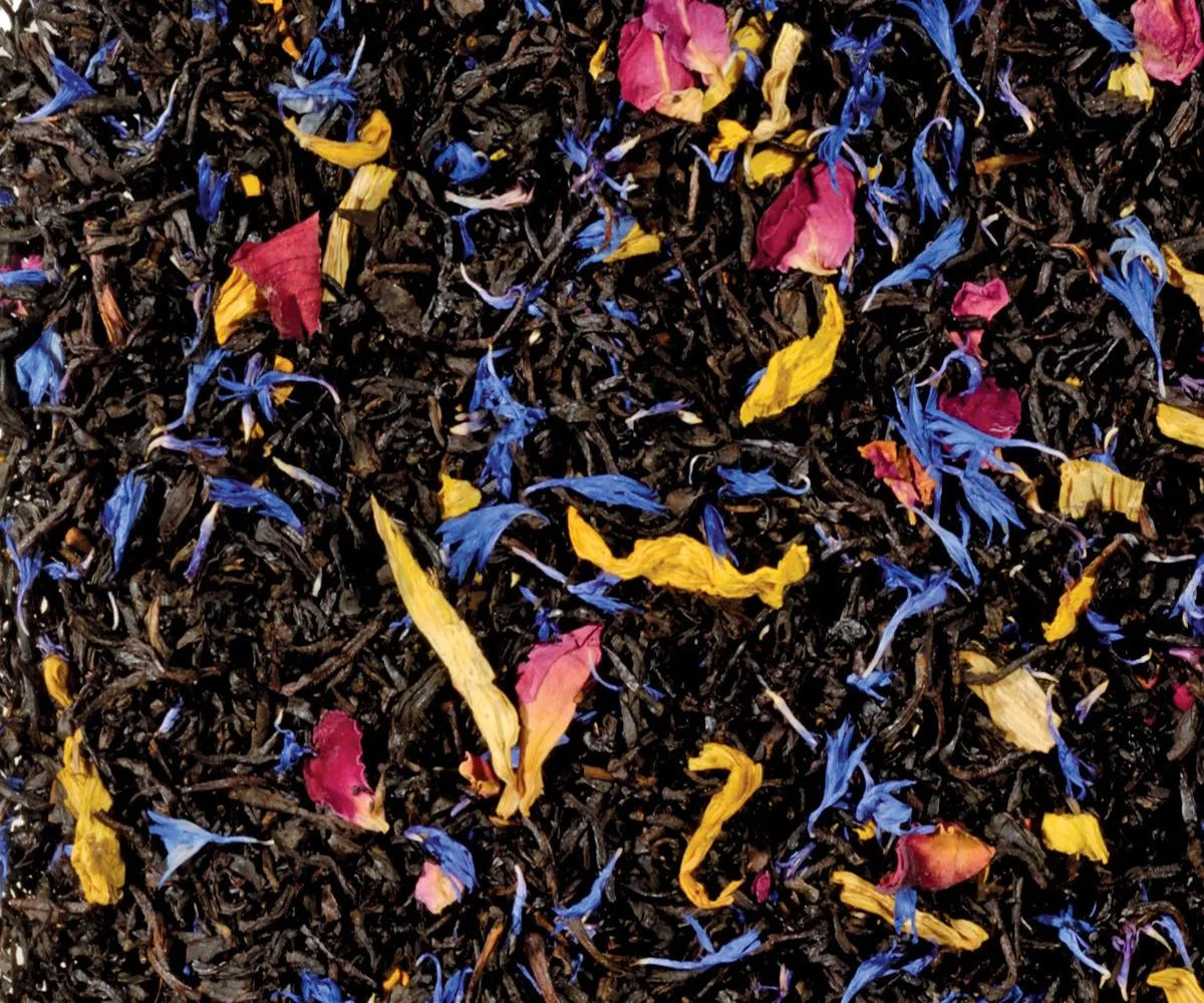 Freigestellte Nahaufnahme des aromatisierten Schwarztees "Südseezauber" mit Mango, Maracuja und Papaya, verziert mit blauen Kornblumenblüten und Rosenblütenblättern