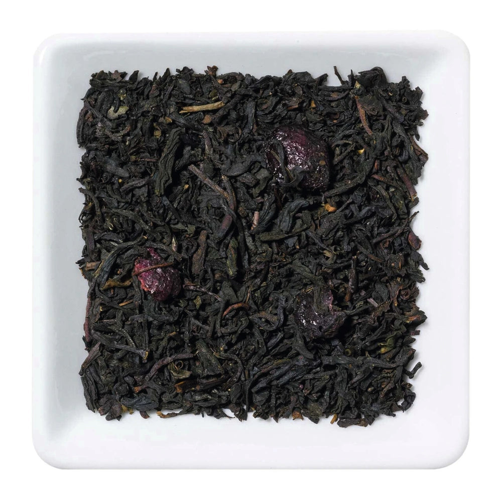 Freigestellte Nahaufnahme des aromatisierten Schwarztees "Wildkirsche" mit Waldbeeren und Kirschstücken.